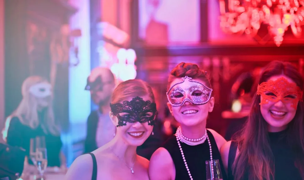 A group of young folks smiling at the camera, wearing masks in a mysterious setting.